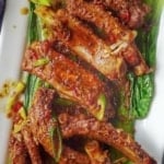 braised pork ribs with black bean sauce over blanched bok choy with overlay text that says black bean ribs
