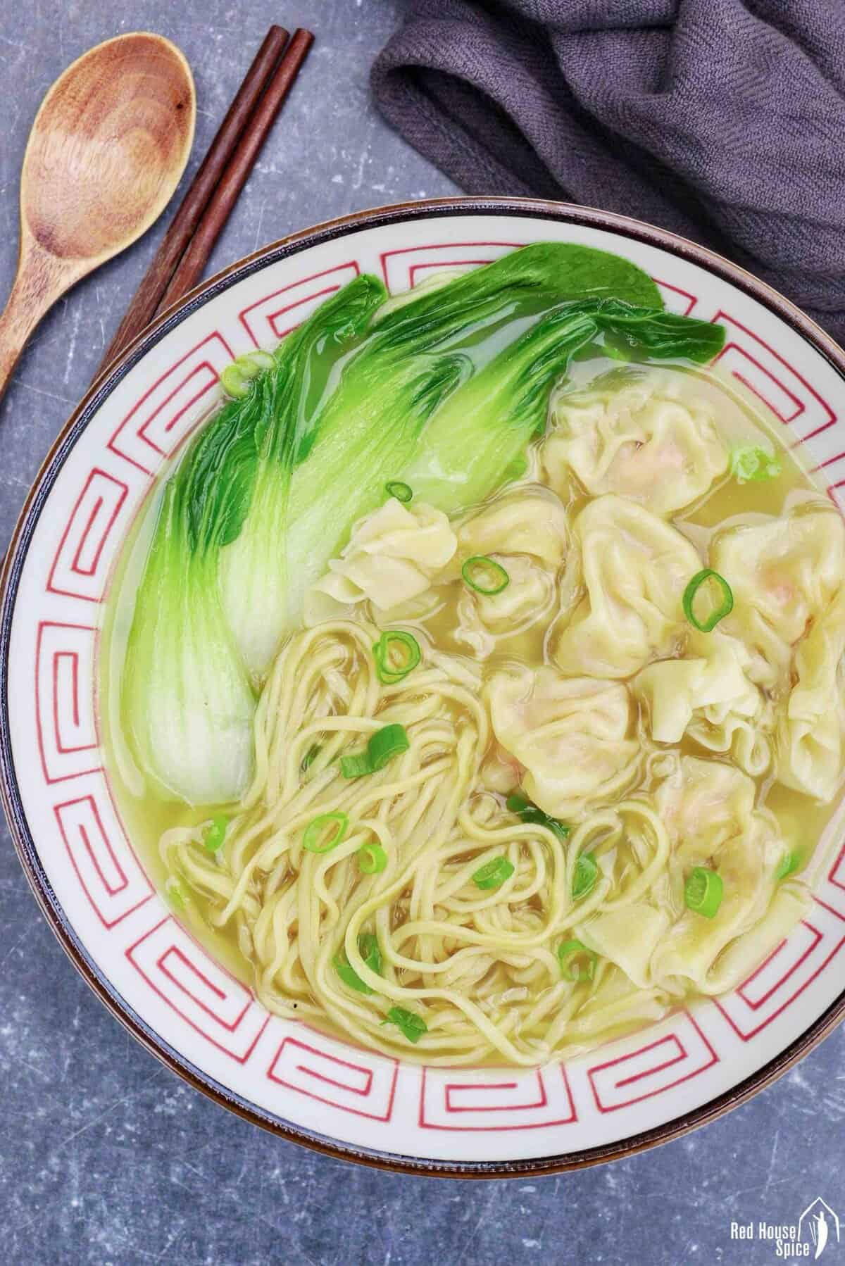 a bowl of wonton noodle soup with bok choy.
