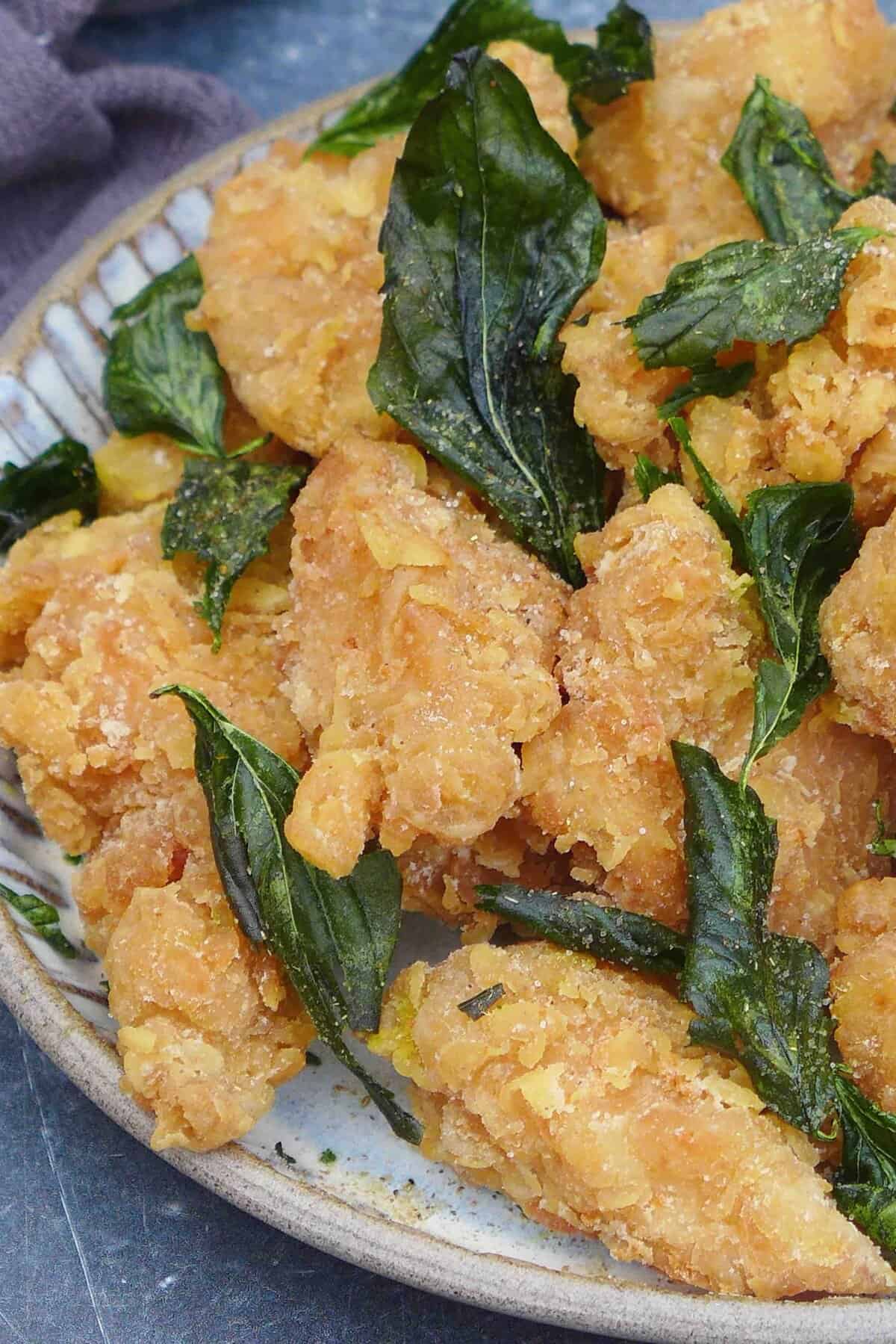 a plate of popcorn chicken with fried basil leaves.