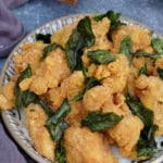 a plate of popcorn chicken with fried basil leaves.