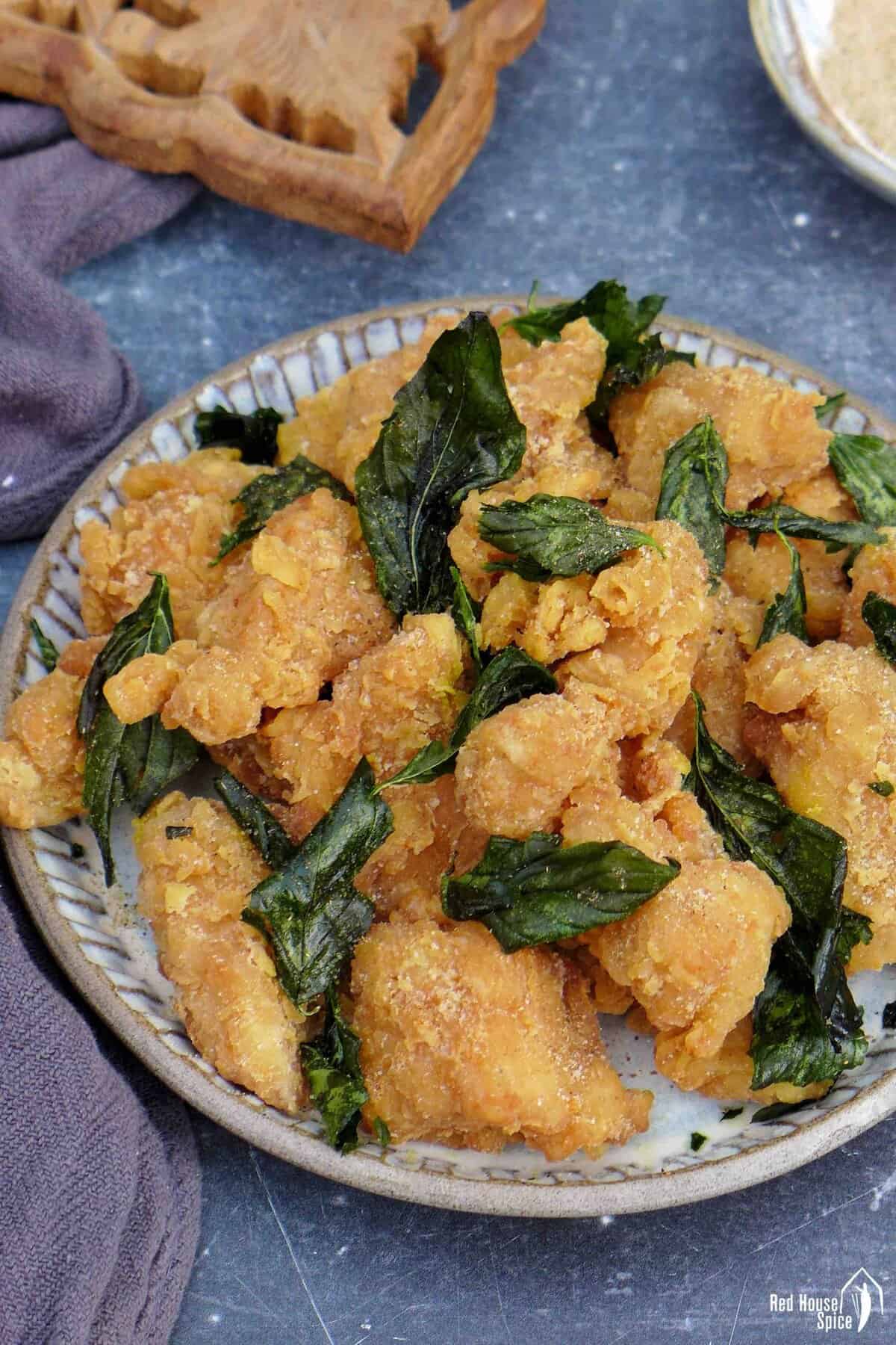 a plate of popcorn chicken with fried basil leaves.