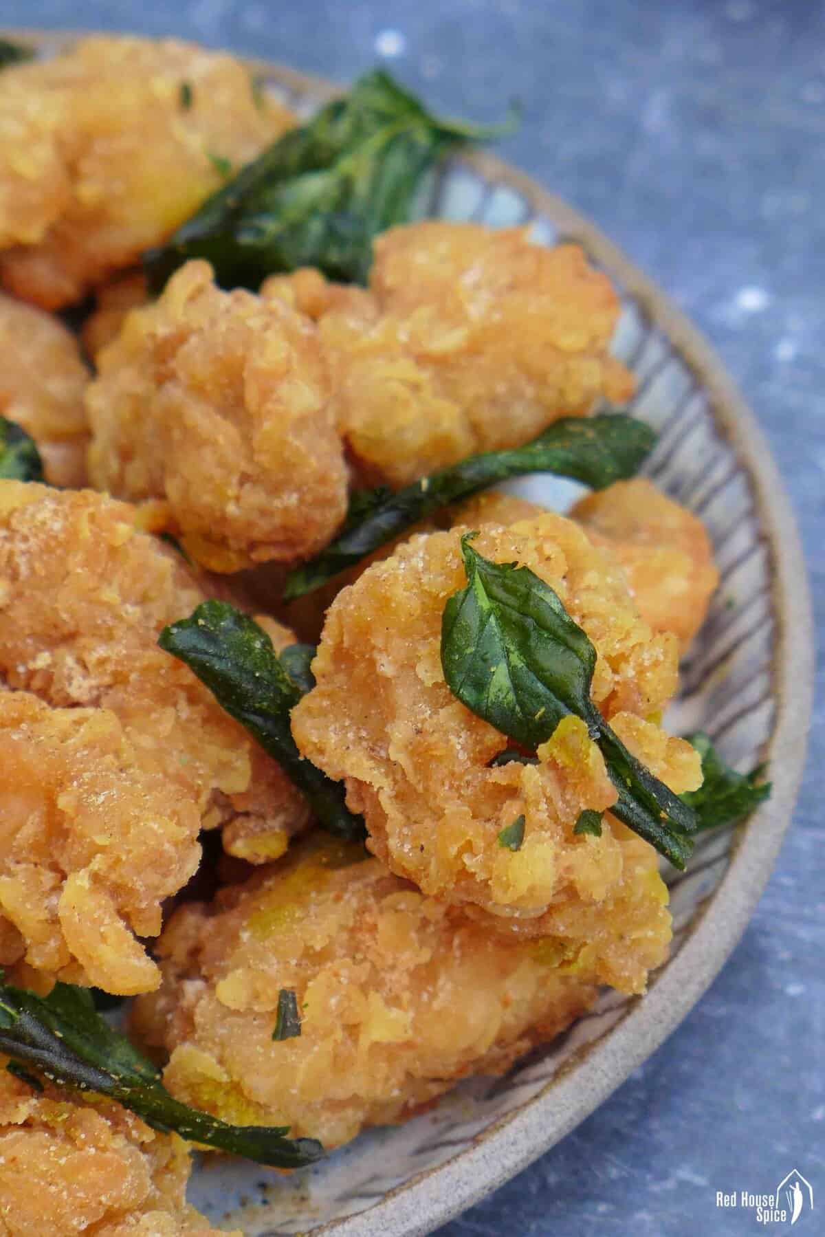 a plate of popcorn chicken with fried basil leaves.